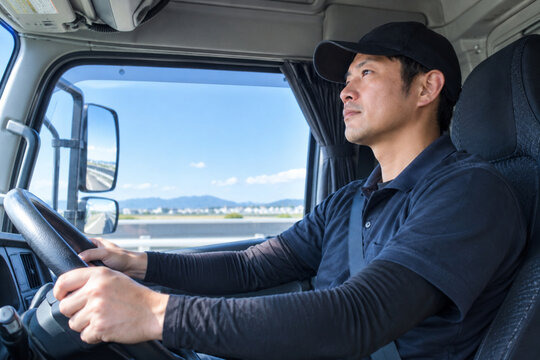 トラックを運転する男性ドライバーの車内ショット/Side view of a Japanese male driver inside a vehicle driving on a sunny day