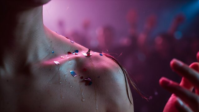 Close-up of a woman's shoulder and neck with water droplets and glitter in colorful party lighting