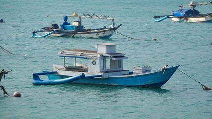 Traditional wooden outrigger fishing boats anchored in the calm turquoise waters of a tropical ocean bay, showcasing local maritime culture and artisanal fishing vessels in Southeast Asia. © Silmiart
