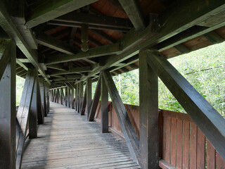 Covered wooden bridge near Obstfelderschmiede in the Schwarza Valley. Massive wooden beams, diagonal braces, and recurring structural elements form a geometric framework with a striking perspective. © Frank