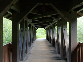 Covered wooden bridge near Obstfelderschmiede in the Schwarza Valley. Massive wooden beams, diagonal braces, and recurring structural elements form a geometric framework with a striking perspective. © Frank