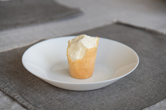 A partially eaten vanilla ice cream cone with visible bite marks stands upright on a white plate.