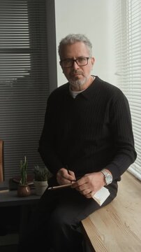 Portrait of middle aged Caucasian psychotherapist taking notes in notepad, looking at camera in office. Clip suitable for corporate training and leadership marketing, vertical