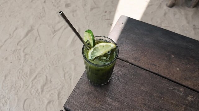 A refreshing green iced drink with lemon and lime slices in a glass on a wooden table, summer vacation, tropical beach vibes, cold beverage, holiday refreshment, relaxing outdoors, sunny day mood