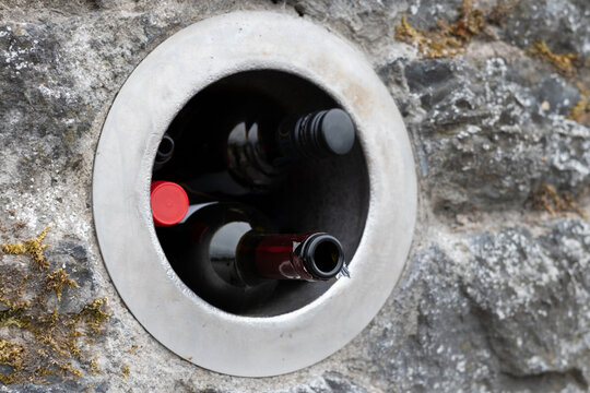 Brown glass wine bottles lie in special hole in the wall for recycling, people hand over bottles, cans, and glass here for further recycling and use