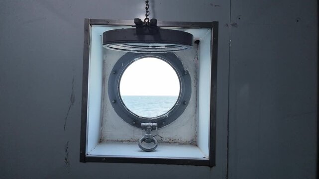 Circular ship porthole window frame opening to vast blue ocean view, metallic industrial bulkhead wall texture, nautical maritime travel transportation, ocean voyage experience