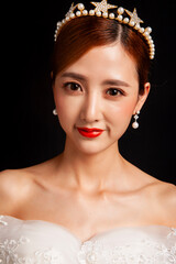 An elegant East Asian bride wearing an off-the-shoulder white lace wedding gown and a star-shaped pearl tiara, set against a solid black background. © jeson