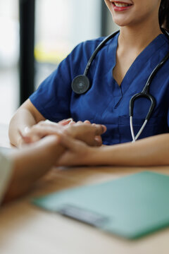 Healthcare worker wearing blue scrubs and a stethoscope offering a comforting hand to a patient, conveying support, compassion, and a positive relationship in a medical setting