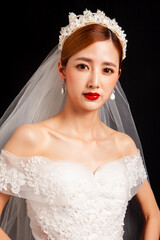 An elegant East Asian bride wearing an off-the-shoulder white lace wedding gown and a star-shaped pearl tiara, set against a solid black background. © jeson