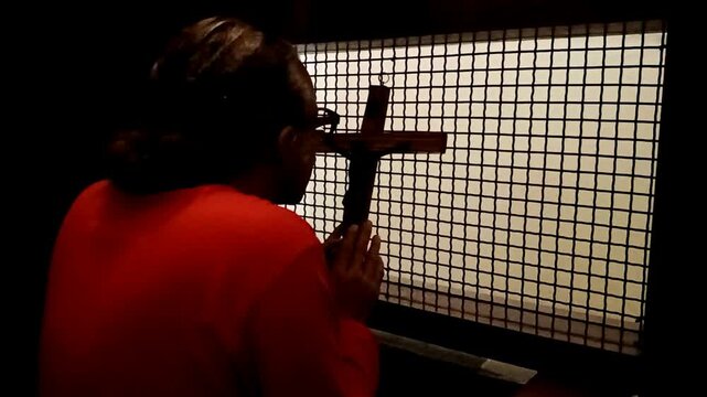 A man confesses his sins in front of the cross of Jesus Christ in the confession room.