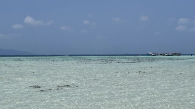Clear turquoise tropical sea water at Cemara Kecil island with coral reef visible beneath surface and distant mountain horizon, perfect for travel, summer vacation, nature tourism, marine life