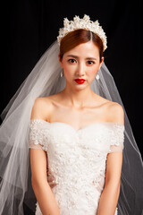 An elegant East Asian bride wearing an off-the-shoulder white lace wedding gown and a star-shaped pearl tiara, set against a solid black background. © jeson