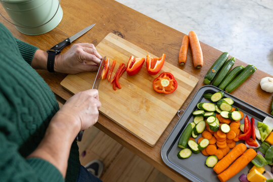 Asian man slicing red bell pepper with chef's knife on bamboo cutting board, copy space