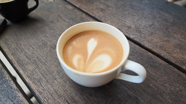 Close up of a freshly brewed cappuccino with delicate heart latte art in a white ceramic cup, steam rising, perfect for caf&eacute; atmosphere or coffee shop advertisement, morning routine
