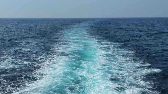 Deep blue ocean wake trailing behind a speeding boat, churning white water ripples, turquoise foam textures, vast horizon line, peaceful marine scenery, summer travel serenity