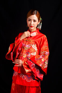 A young East Asian woman, dressed in exquisite traditional Chinese wedding attire and wearing classic hair accessories and makeup featuring red lips, embodies a festive wedding fashion style against a