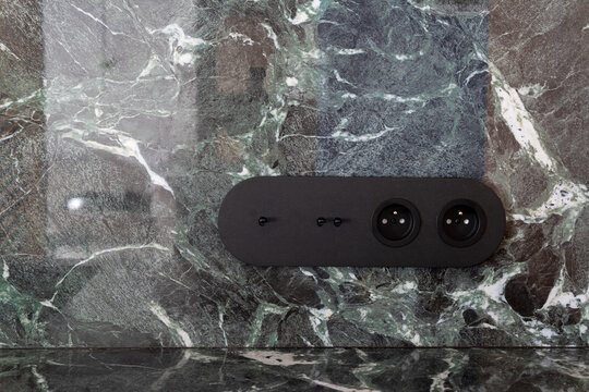 Modern black electric socket and light switch on green marble wall