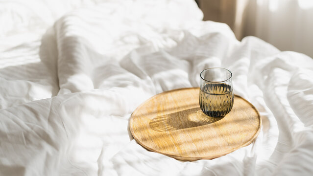 Glass of water on wooden tray on white bed linen