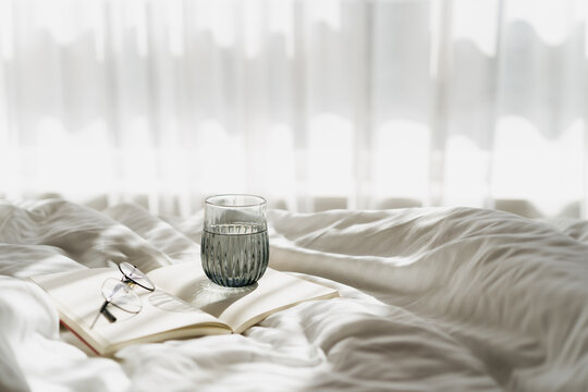 Open book and water glass on white bed linen