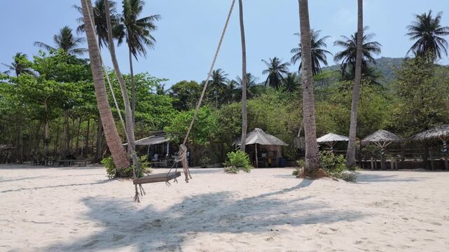 Empty wooden swing hanging from coconut palm on tropical beach, serene shoreline with lush vegetation, thatched huts, summer getaway, vacation relaxation, travel leisure, paradise landscape