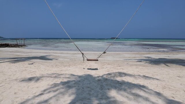 Empty wooden swing hanging on ropes at pristine tropical sandy beach with calm ocean water, summer vacation mood, perfect for travel storytelling and relaxation atmosphere, serene paradise scenery