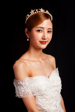 An elegant East Asian bride wearing an off-the-shoulder white lace wedding gown and a star-shaped pearl tiara, set against a solid black background.