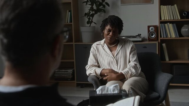 African American young adult woman talking to therapist during counseling session, over shoulder view. Clip ideal for mental health awareness campaigns and psychology service promotions
