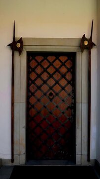 Close-up vertical video of an old historic door decorated with a forged metal lattice and ornamental iron pikes set in a stone portal. 