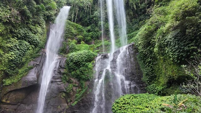 Sekumpul waterfall cascading down tropical cliffs in Bali, lush jungle foliage and vibrant green moss, serene atmosphere and powerful water flow for travel documentaries and nature relaxation videos
