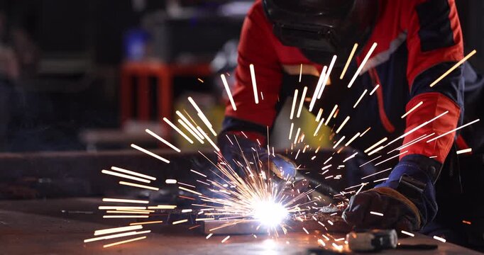 Welder wearing a protective welding helmet, gloves, and workwear performs a test weld on steel at a workbench.