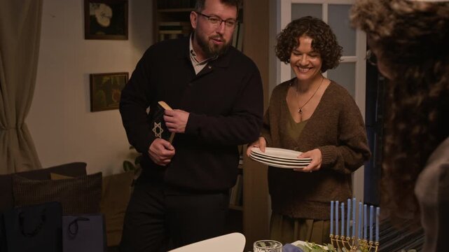 Caucasian family setting dinner table with menorah and dishes for Hanukkah celebration. Clip suitable for Jewish holiday campaigns and cultural lifestyle content