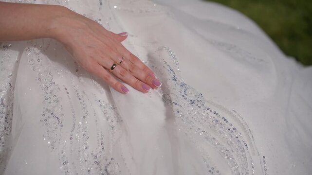Bride hand with gold wedding ring on beaded white dress