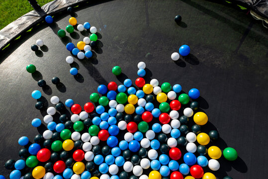 Colorful plastic balls scattered on black trampoline surface