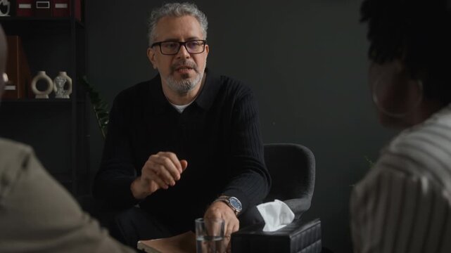 Middle aged Caucasian therapist counseling couple during therapy session, gesturing and explaining mental health advice. Footage suitable for marriage counseling ads and psychotherapy promotions