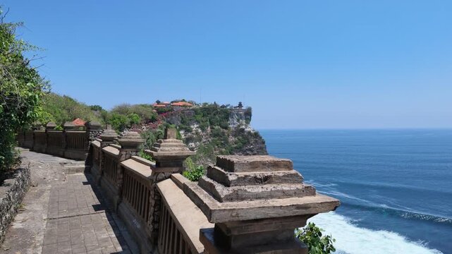 Stone path along Uluwatu temple cliffs overlooking deep blue ocean waves, traditional Balinese architecture, tropical coastline scenery, serene travel destination, vacation summer vibes