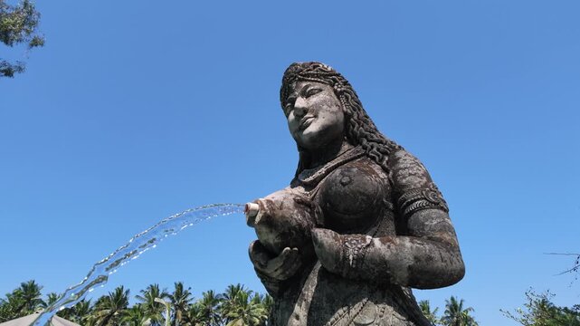 Stone statue of woman fountain spraying water in Ubud Bali, traditional Balinese temple sculpture, religious pilgrimage site, spiritual landmark, peaceful atmosphere, tropical landscape. Solw motion