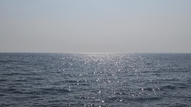 Sunlight glittering on the calm blue ocean surface, rippling waves reflecting rays, serene tropical sea waters, calming nature background for travel and wellness