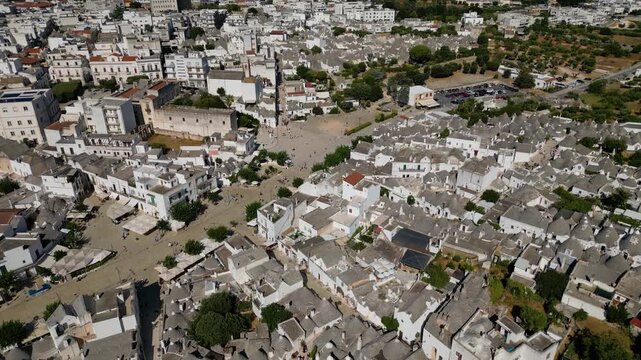 A breathtaking high aerial view of Alberobello in Puglia, Italy, revealing thousands of iconic white trulli huts with conical stone roofs. The historic UNESCO town stretches across the landscape