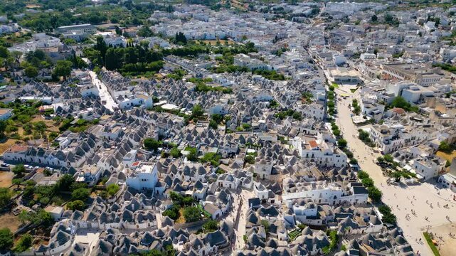 A breathtaking high aerial view of Alberobello in Puglia, Italy, revealing thousands of iconic white trulli huts with conical stone roofs. The historic UNESCO town stretches across the landscape