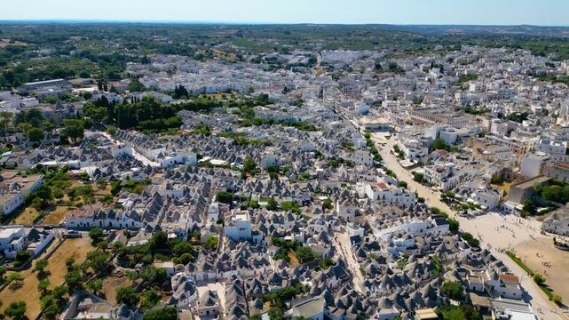 A breathtaking high aerial view of Alberobello in Puglia, Italy, revealing thousands of iconic white trulli huts with conical stone roofs. The historic UNESCO town stretches across the landscape