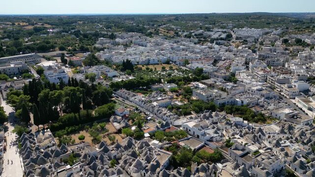 A breathtaking high aerial view of Alberobello in Puglia, Italy, revealing thousands of iconic white trulli huts with conical stone roofs. The historic UNESCO town stretches across the landscape