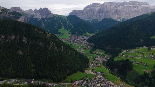 Slow aerial drift over Val Gardena valley toward Selva with Sella group and Cir peaks under overcast sky, Dolomites, South Tyrol, Alps, Italy