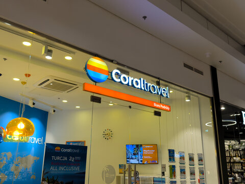 Illuminated travel agency storefront with colorful sunset logo sign inside a modern shopping mall, featuring glass doors, bright interior lighting and vacation promotions