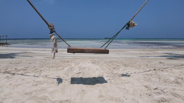 Wooden beach swing suspended by ropes over white sand, tropical island scenery with calm turquoise ocean, summer vacation vibe, peaceful paradise escape, travel destination relaxation