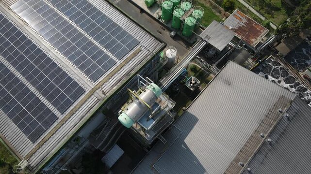 Aerial view of solar panels installed on a factory roof with industrial water treatment tanks and pipes in Banyumas Regency, Central Java, Indonesia.