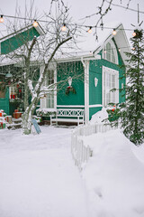 Obraz premium Vertical shot of snow covered wooden house decorated with Christmas lights and festive ornaments. Exterior winter scene suitable for holiday seasonal advertising and travel marketing