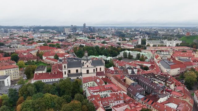 Drone video captures Vilnius Old Town&rsquo;s charming red rooftops, baroque churches, lush greenery, and urban skyline under overcast daylight, highlighting its unique architectural landscape.