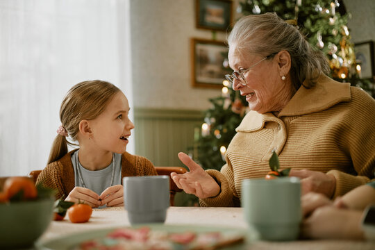 Senior Caucasian grandmother talking with granddaughter at dining table during Christmas holiday. Image representing intergenerational bonding, ideal for family insurance advertising