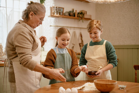 Senior Caucasian woman teaching Caucasian girl and boy baking in kitchen. Scene suitable for family lifestyle advertising, cooking workshops, holiday culinary campaigns