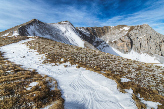 View of the snow-covered slopes and rocky peaks of Monte Vettore under a clear blue sky in the Apennine Mountains, Monte Vettore, Marche, Italy.